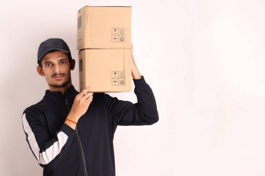 Kahverengi kutulu, siyah tişörtlü, beyaz arka planda yüz ifadeleri olan, traşsız Hintli kurye çocuk. 