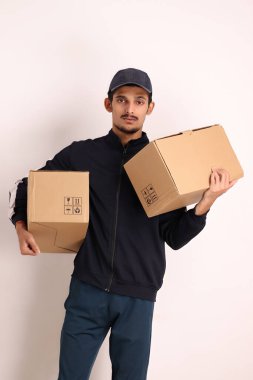 Kahverengi kutulu, siyah tişörtlü, beyaz arka planda yüz ifadeleri olan, traşsız Hintli kurye çocuk. 