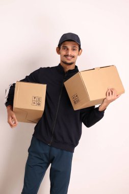 Kahverengi kutulu, siyah tişörtlü, beyaz arka planda yüz ifadeleri olan, traşsız Hintli kurye çocuk. 