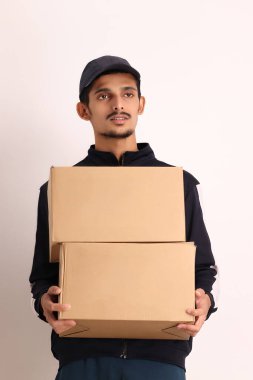 Kahverengi kutulu, siyah tişörtlü, beyaz arka planda yüz ifadeleri olan, traşsız Hintli kurye çocuk. 