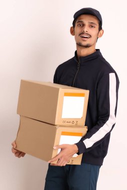 Kahverengi kutulu, siyah tişörtlü, beyaz arka planda yüz ifadeleri olan, traşsız Hintli kurye çocuk. 