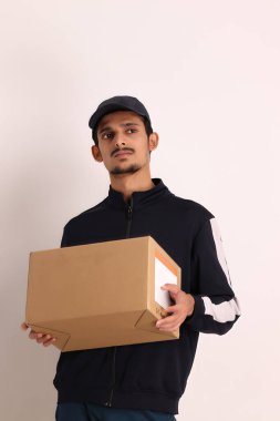 Kahverengi kutulu, siyah tişörtlü, beyaz arka planda yüz ifadeleri olan, traşsız Hintli kurye çocuk. 