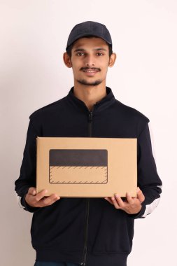 Kahverengi kutulu, siyah tişörtlü, beyaz arka planda yüz ifadeleri olan, traşsız Hintli kurye çocuk. 