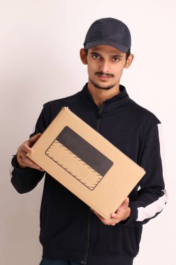 Kahverengi kutulu, siyah tişörtlü, beyaz arka planda yüz ifadeleri olan, traşsız Hintli kurye çocuk. 