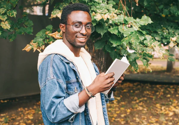 Portret Młodego Afrykańskiego Studenta Książką Odwracającą Wzrok Okularach Jesiennym Parku — Zdjęcie stockowe