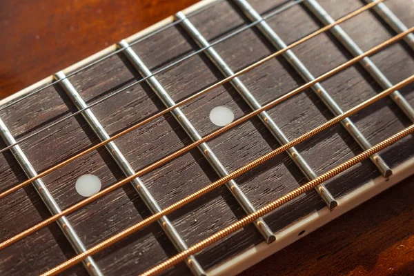 Guitar neck, stretched strings, frets and texture of natural material neck with selective shallow focus.