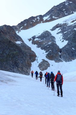 Halat ekibi, Avusturya 'nın Tyrol Alps kentindeki Wildspitze ve dağ kar panoramalarına doğru buzul Taschachferner üzerinde kramponlarla dağcılık yapıyor.
