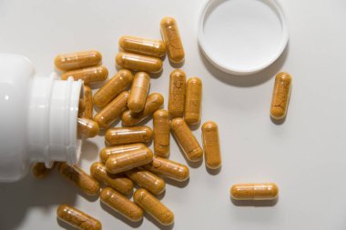 Beyaz zemin üzerinde beyaz bir şişe içinde sarı tozlu şeffaf kapsüller üst görünümü kapatın