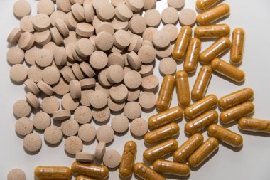 Sarı tozlu şeffaf kapsüller ve beyaz arka planda açık kahverengi haplar. Üst görünümü kapatın.