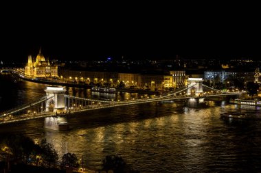Budapeşte 'nin Tuna Nehri üzerindeki Zincir köprüsü ve geceleyin Macaristan' ın Budapeşte kentindeki Parlamento binası üzerindeki manzarası