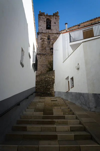 Narrow street of the medieval town of Ares del Maestre with the Church of the Assumption of Our Lady in the background on a blue day, Castellon, Spain