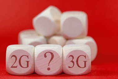 Üzerinde 2G, 3G yazıları olan tahta küpler, kırmızı arkaplan önünde soru işareti