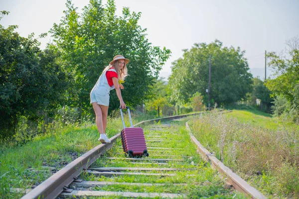 Şapkalı bir kız tren yolu boyunca bavuluyla yürüyor. — Stok fotoğraf