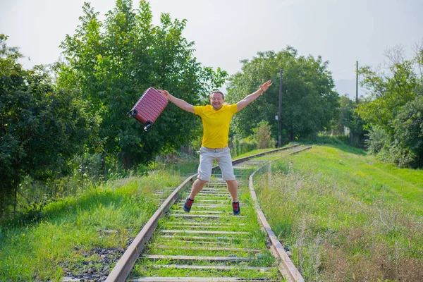 Şortlu ve bavullu bir adam demiryoluna atlıyor. — Stok fotoğraf