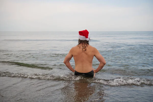 En man klädd i en jultomte hatt vid havet — Stockfoto