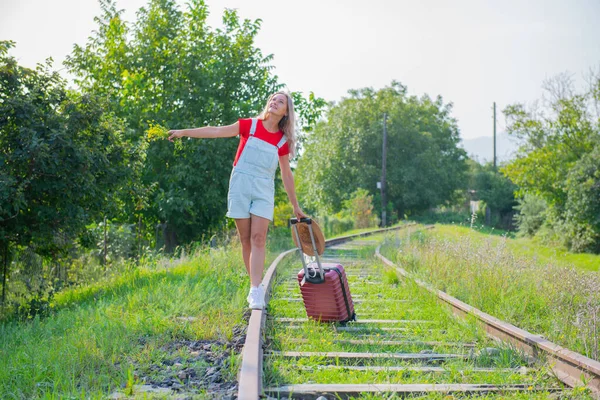 Happy woman with hat walking on rails with suitcase — Stock Photo, Image