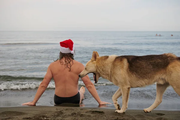 En man klädd i en jultomte hatt vid havet — Stockfoto