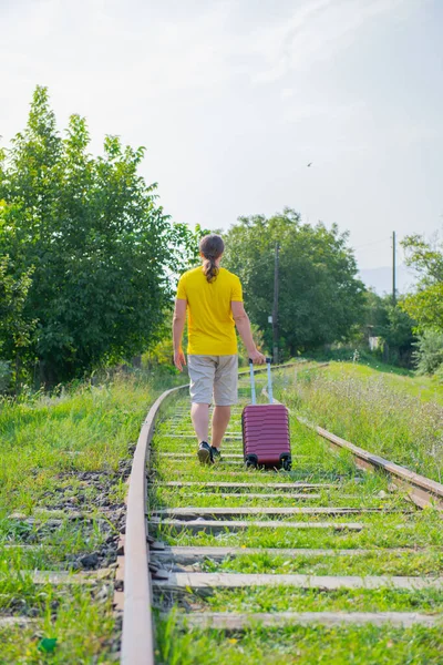 Мужчина в жёлтой футболке ходит по рельсам с чемоданом — стоковое фото
