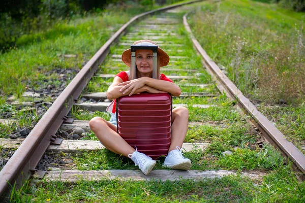 Um viajante usando um chapéu senta-se em trilhos com uma mala — Fotografia de Stock