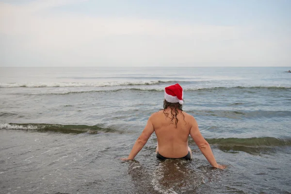 En man klädd i en jultomte hatt vid havet — Stockfoto