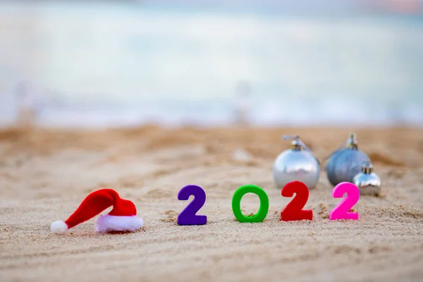 Santa Claus sombrero 2022 números se encuentran en la arena junto a los regalos — Foto de Stock