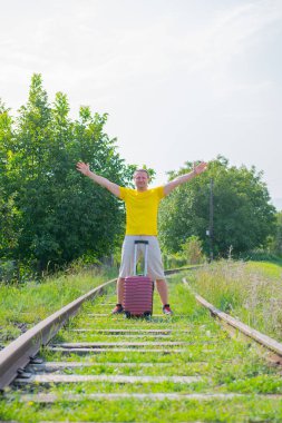 Esmer çocuk elinde bavulla demiryolunda yürüyor.