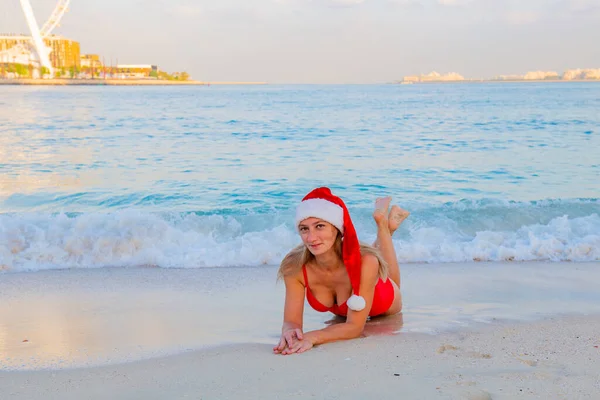 At the sea a girl in a Christmas hat lies in a bikini — Stockfoto