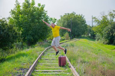 a man with a red suitcase jumping on the railroad