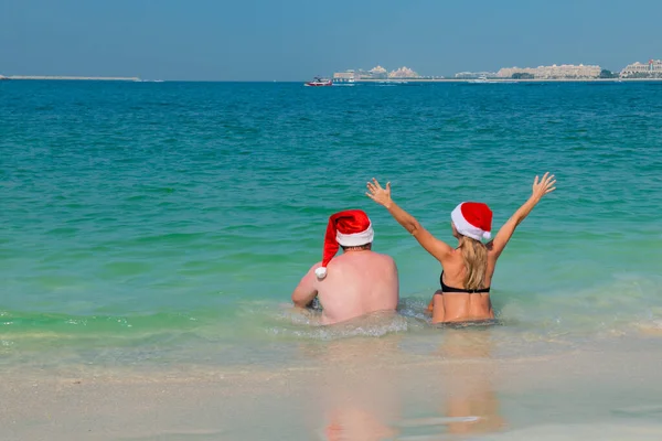 На пляжі жирний чоловік сидить на морі в новорічному капелюсі — стокове фото