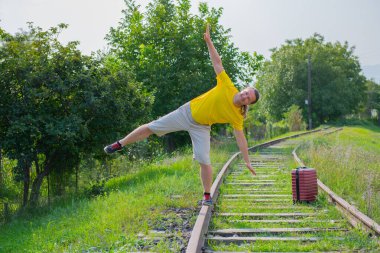 a grimacing traveler with a suitcase walks along the rails