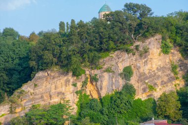 Tepesinde kale olan yeşillikle kaplı bir kaya.