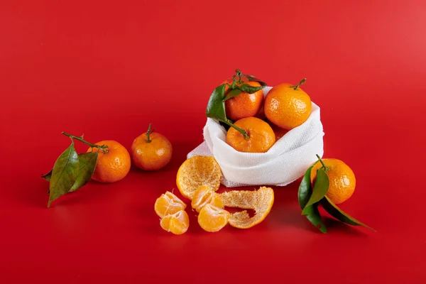 Kırmızı arka planda mandalina dilimleri ve beyaz bir çanta.