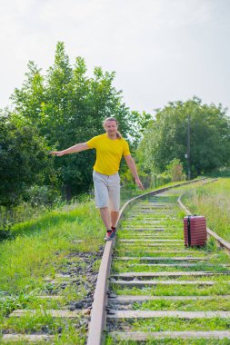 Raylarda kırmızı bavullu havalı gezgin gider.