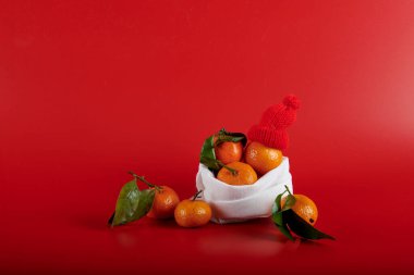 Kırmızı arka planda mandalinalı çanta ve Noel Baba şapkası.