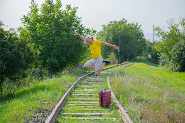 Kırmızı bavullu yalnız bir adam demiryoluna atlıyor.