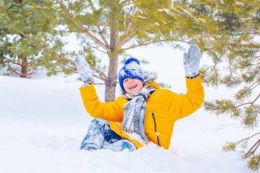Çok parlak sarı ceketli ve mavi şapkalı bir çocuk karda oynuyor.