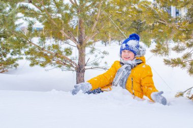 Sarı ceketli ve mavi şapkalı bir çocuk karda oynuyor.