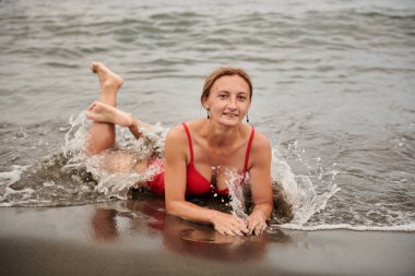 Kırmızı mayolu mutlu kız deniz kıyısında yatıyor.