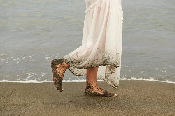womens feet in the sand nai white dress on the beach
