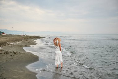 Şapkalı ve beyaz elbiseli bir kız sahilde yürüyor. Yüksek kalite fotoğraf