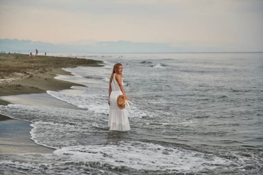 Sırtında beyaz elbiseli bir kızla kıyıda duruyor. Yüksek kalite fotoğraf