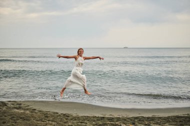 Plaj kızına atlarken ellerini yanlarına koy. Yüksek kalite fotoğraf