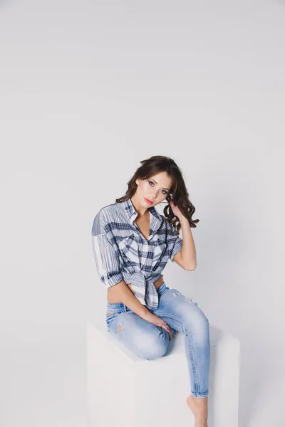 Una Ragazza Camicia Quadri Jeans Siede Cubo Bianco Uno Sfondo — Foto Stock