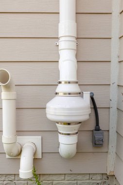 PVC pipes attached to the electrical motor of a residential radon mitigation system. TIt sucks radon rich basement ground air and removes it from the top of the house. Also helps with humidity