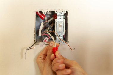 Bir elektrikçi bir elektrik düğmesini değiştiriyor. Bir DIY proje konsepti. Yüksek voltaj tehlikesi. Plastik kablo kullanarak çıplak elle sıkılaştırma kablolarıyla çalışıyor. Her kabloda etiket var. 