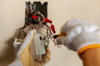Bir elektrikçi bir elektrik düğmesini değiştiriyor. Bir DIY proje konsepti. Yüksek voltaj tehlikesi. Tornavida kullanarak kablo bağlantısı kuruluyor. Profesyonel güvenlik için koruyucu lastik eldiven giyer.