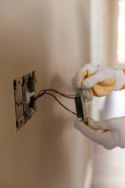 Bir elektrikçi bir elektrik düğmesini değiştiriyor. Bir DIY proje konsepti. Yüksek voltaj tehlikesi. Profesyonel, şok önleme için lastik güvenlik eldiveni giyiyor. İzole edilmiş kapatma resmi