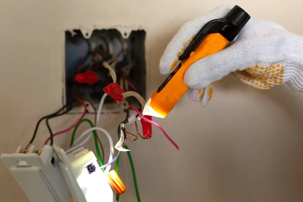 Bir elektrikçi bir elektrik düğmesini değiştiriyor. Bir DIY proje konsepti. Yüksek voltaj tehlikesi. Dokunulmaz bir voltaj ölçer ve koruyucu lastik eldivenler kullanılır. Testçide aydınlatma için fener var.