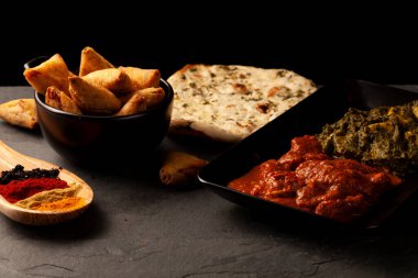 Hindistan 'dan gelen lezzetli yemeklerle dolu bir masa resmi. Naan, körili tavuk, palak paneer, samosa, çeşitli baharatlar ve taş üzerinde tatlandırıcılarla düşük açık renk arka plan.