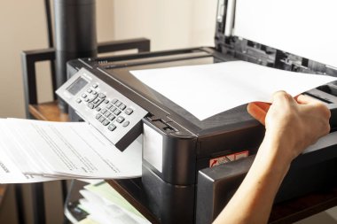 Ofis işleri için imaj kavramı. Bir kadın kağıt yerleştiriyor ya da çıkarıyor. Küçük bir ofis ayarında rafların üstünde kablosuz fotokopi, tarayıcı ve yazıcı kombinasyonu cihazı var.. 